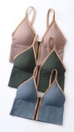 Drie geribde bralettes met rits vooraan in stofroze, dennengroen en leisteenblauw met beige bies, plat gelegd.